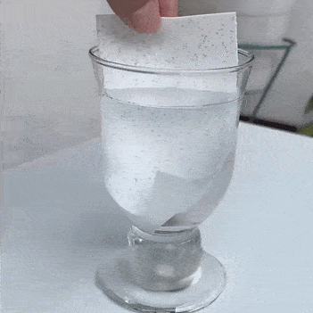 Hoja de detergente Nuvy disolviéndose en agua dentro de una copa; se disuelve en segundos y no deja residuos, ideal para viaje.