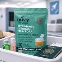 Detergente en hojas Nuvy by Drynest para viaje, mostrado en charola de aeropuerto junto a artículos de mano.